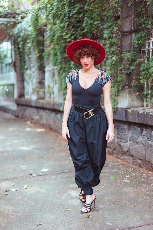 Stylish woman in black outfit wearing a contrasting red hat on a leafy city street