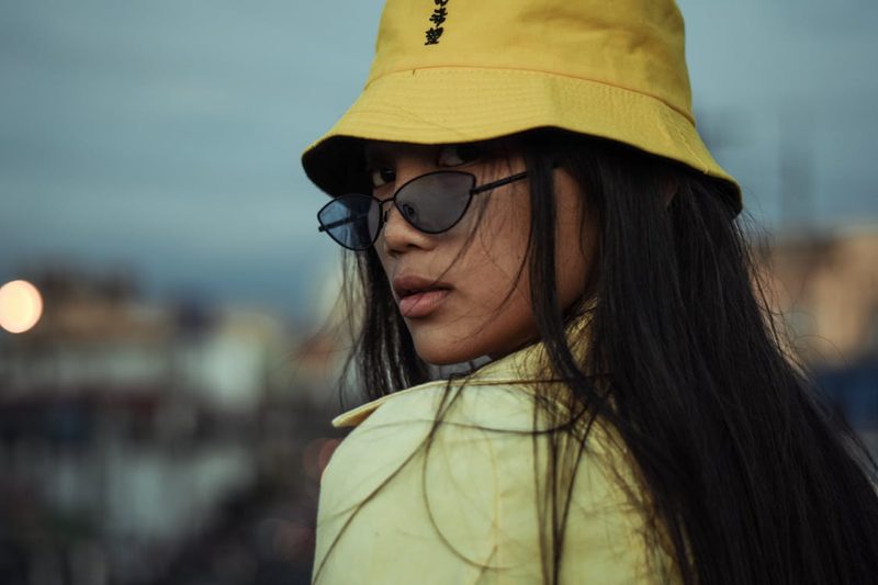 Fashion-forward woman wearing a bright yellow bucket hat and sunglasses making a bold optimistic style statement