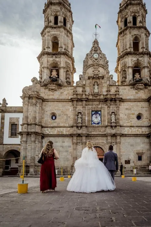 Bride approaching a church entrance for a wedding ceremony where guest hats complete the scene