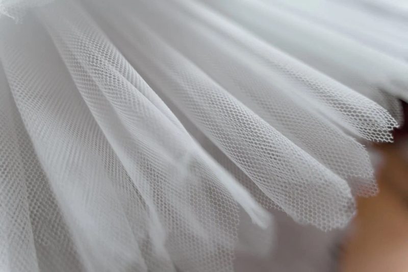 Delicate white tulle fabric in close-up showing the fine mesh texture used in fascinators, veils, and christening headpieces
