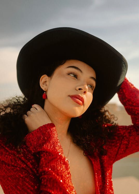 Elegant woman in a red sequin outfit and black formal hat posing in a studio portrait