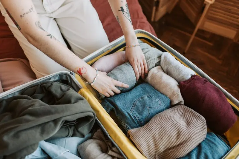 Person carefully packing items into luggage demonstrating travel packing techniques for hats