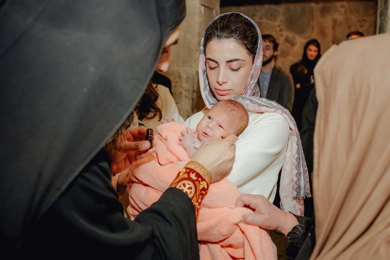 Mother tenderly holding her baby in a white christening gown during a baptism ceremony at a church