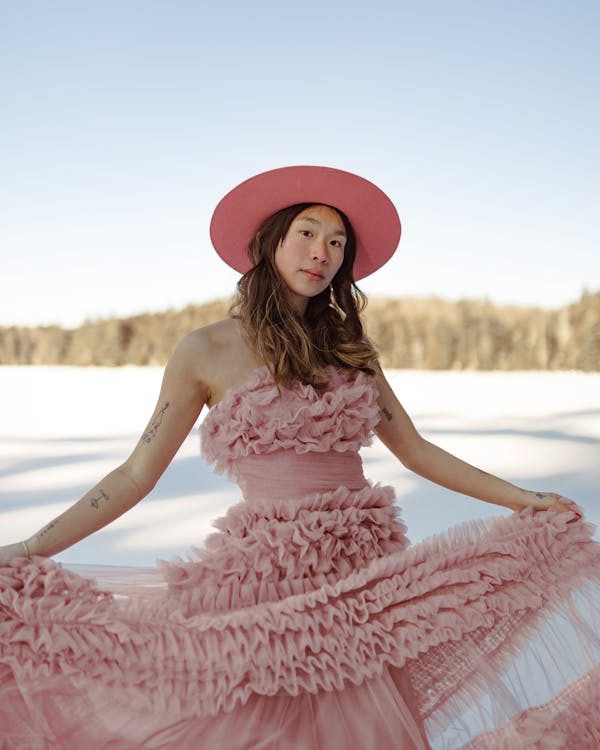 Woman in coordinated pink dress and matching hat posing against a winter backdrop