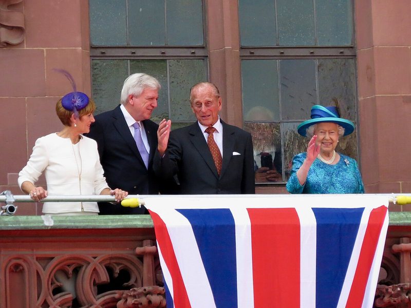 Queen Elizabeth II wearing one of her signature colourful blue hats during a state visit, known for her lifelong love of millinery