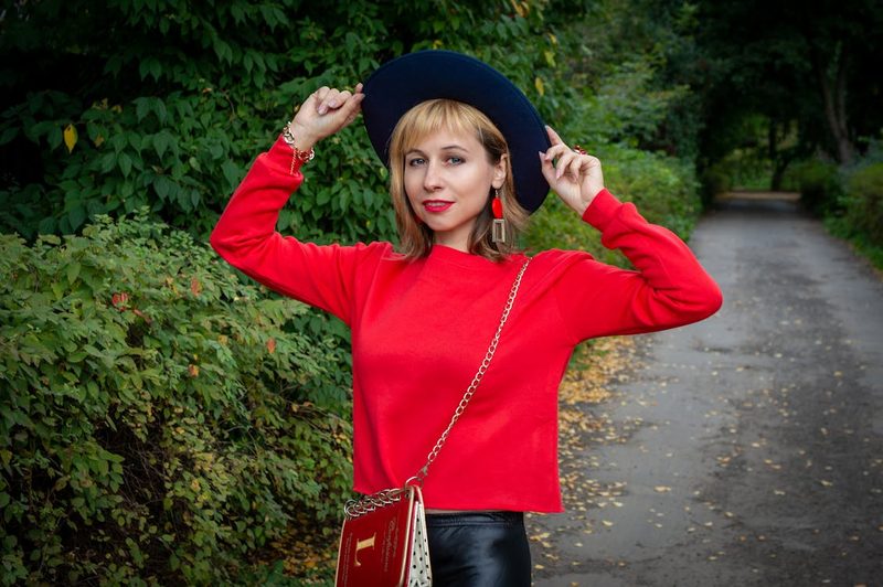 Woman in red long sleeve top wearing a complementary black hat among autumn foliage