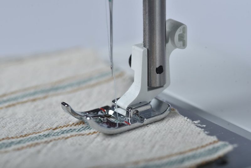 Sewing machine needle and presser foot on fabric representing the precision tools used in millinery