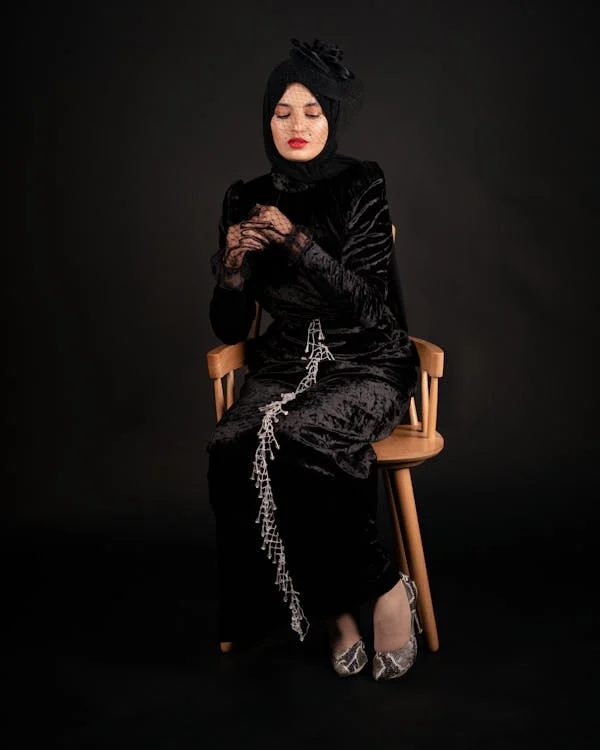 Model in a long black satin dress wearing a small fascinator headpiece with veil demonstrating how a minimal cocktail hat can complete a race day look