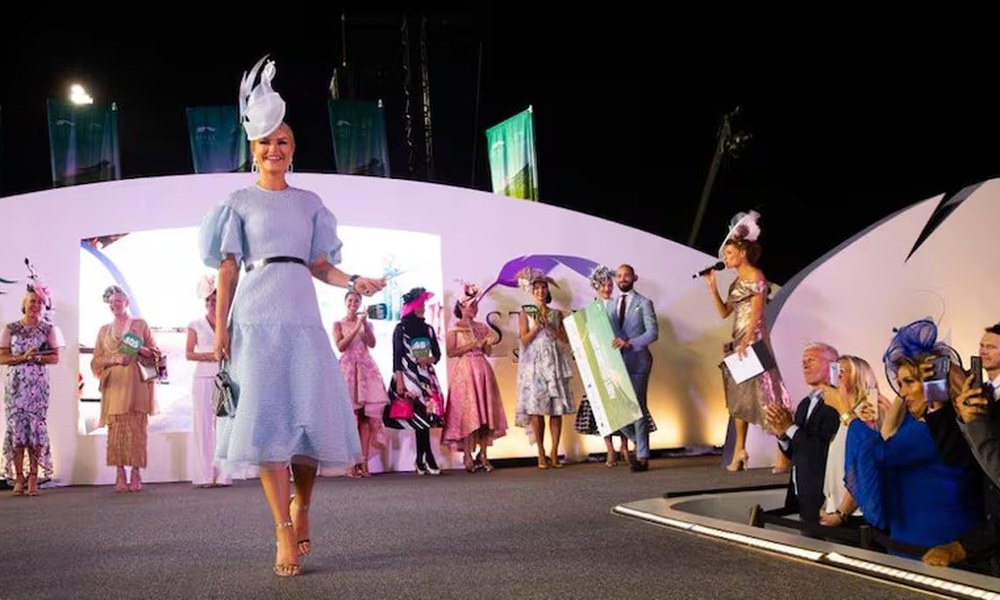 Fashions on the Field winner walking the catwalk in powder blue dress and white sculptural hat at spring racing carnival