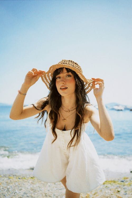Young woman wearing a straw hat and dress enjoying a sunny day by the seaside