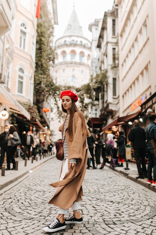 Woman in brown trench coat and red hat standing on a cobblestone street showcasing tonal coordination