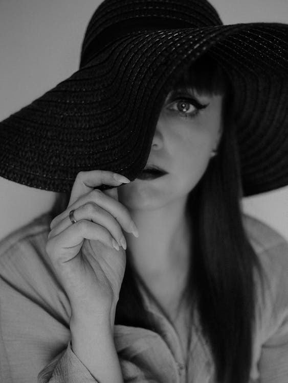 Black and white portrait of woman looking from under a wide-brimmed hat conveying elegance and mystery