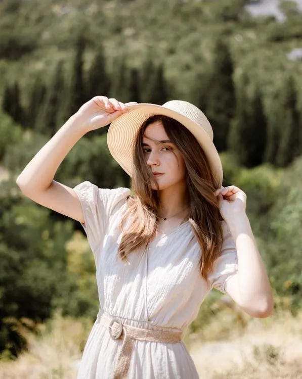 Stylish woman in a white summer dress and wide-brim hat posing outdoors in the sunlight