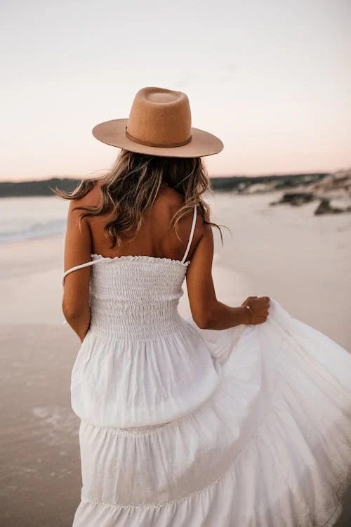 Woman in a white dress and elegant wide-brim hat at golden hour showcasing timeless summer style