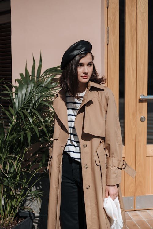 Fashionable woman in a brown trench coat and black beret hat standing outdoors