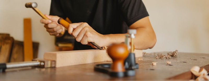 Artisan using hand tools to shape wood in a workshop showcasing traditional woodworking craftsmanship