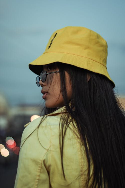 Woman in sunglasses wearing a yellow bucket hat in a vibrant street style fashion portrait
