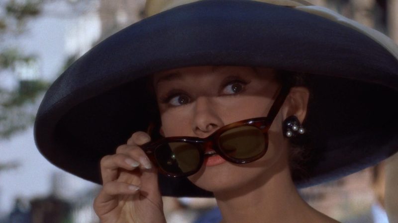Audrey Hepburn wearing her iconic wide-brimmed hat and sunglasses in Breakfast at Tiffanys 1961, one of the most famous hats in cinema history