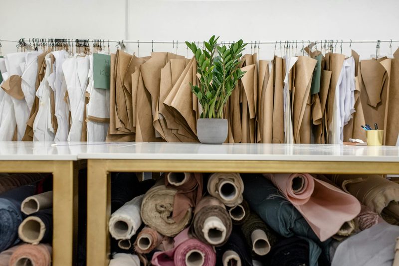 Fashion design atelier with rolls of fabric in soft tones and paper patterns hanging on a rail, evoking the creative workspace of a milliner