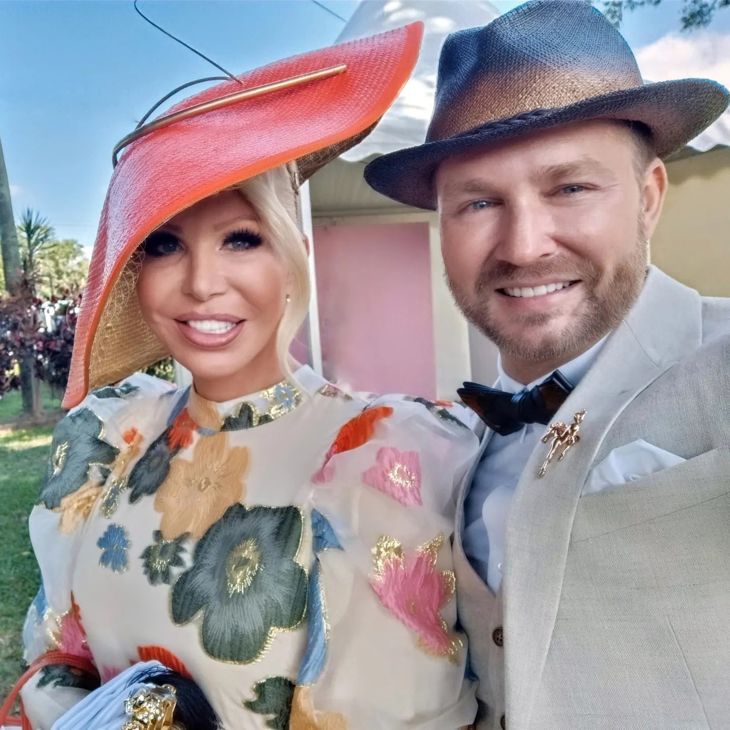 Couple at the races wearing Kathryn Lee Millinery hats - orange wide brim straw hat and navy fedora at spring racing