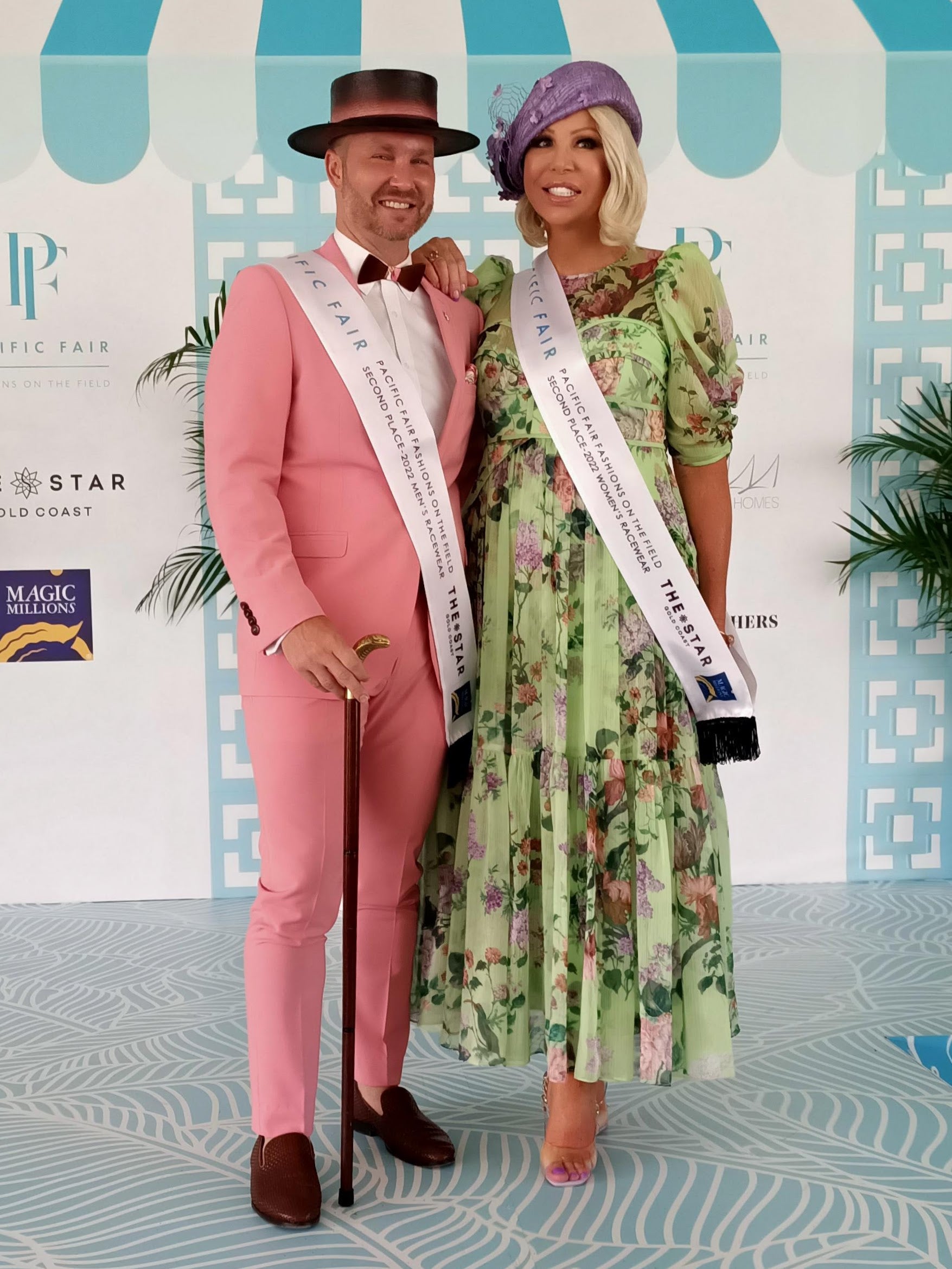 Couple at Magic Millions Gold Coast race day wearing Kathryn Lee Millinery hats with Pacific Fair fashions on the field sashes